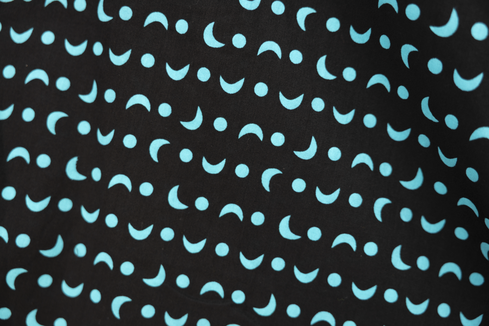 Close up display of sleeveless black dress with teal moon design.