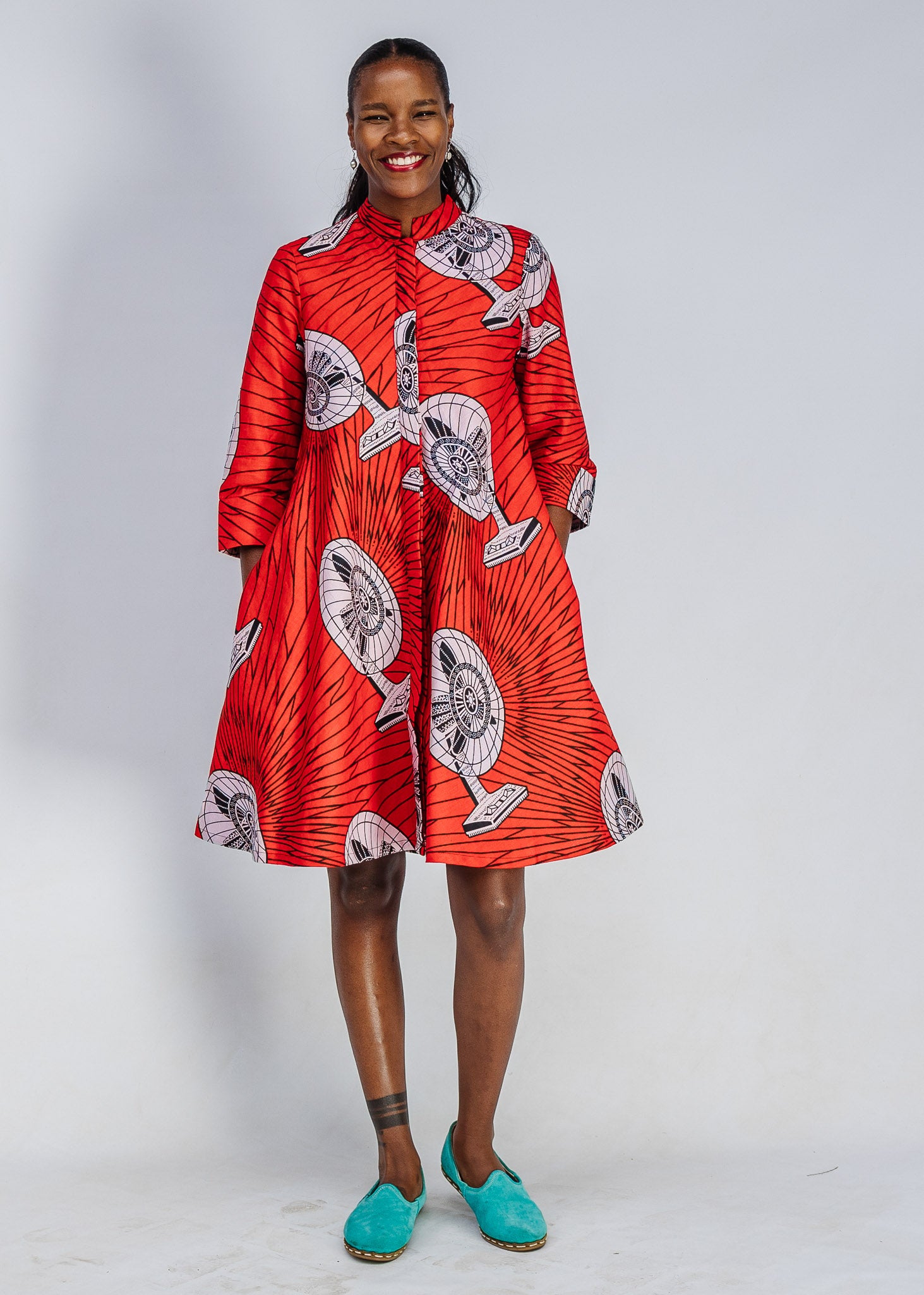Woman wearing a red patterned dress with teal shoes on a white background